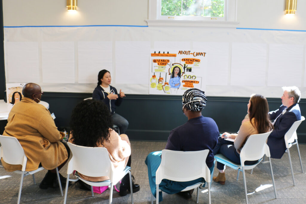 A circle of people sitting, talking, discussing topics on a whiteboard